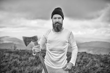 Lumberjack bearded man with axe stand on mountain landscape on cloudy sky. Logging and chopping concept. Wanderlust, vacation, travelling, black and whiteの写真素材
