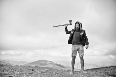 Lumberjack brutal bearded man with axe stand on mountain top on sky background. Achievement, victory, prospect concept. Wanderlust, vacation, travelling, black and whiteの写真素材
