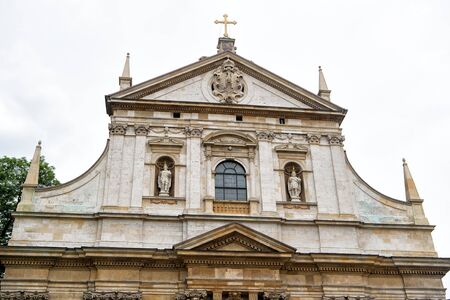 Church facade with cross, statues, masonry ornaments in krakow, poland on grey sky. Architecture, temple, religion conceptの写真素材