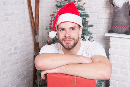Man santa with box at christmas tree. xmas and new year gift giving. Holidays preparation and celebration. Boxing day concept. Macho in red hat with wrapped present.の写真素材