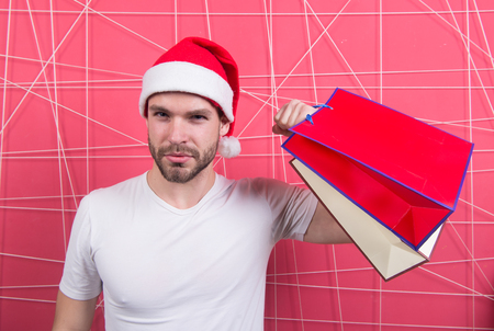 Super santa shopper with paperbags on pink background. Man in xmas hat hold bags in strong hand. Winter sale, shopping concept. Christmas and new year presents. Holidays workout and training.の写真素材