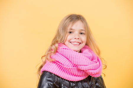 Happy childhood concept. Girl in pink scarf on orange background. Kid beauty, look, hairstyle. Autumn fashion, style, trend. Child model smile with long blond hair.の写真素材