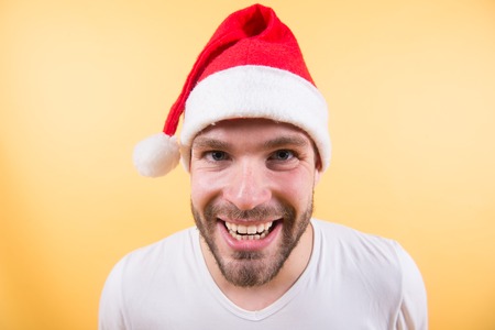 Man santa happy smiling on orange background. Winter holidays celebration concept. Christmas and new year party. Macho in red xmas hat and white tshirt. Santa claus fashion.の写真素材