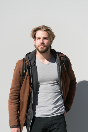 Outfit, fashion, casual style. Man wear brown coat, tshirt, trousers on grey wall. Macho with beard on unshaven face and blond hair.の写真素材
