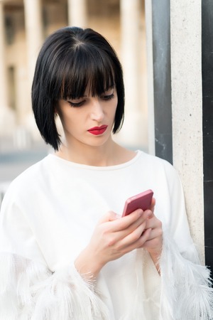 Woman use mobile phone in paris, france. Girl with red lips, brunette hair in white blouse with smartphone. New technology, modern life. Communication, virtual world, sms. Fashion, beauty conceptの写真素材