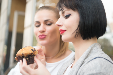 Hunger, temptation, appetite concept. Women look at cupcake in paris, france. Girl friends with blueberry muffin in cafe. Dessert, food, snack, pastry.の写真素材