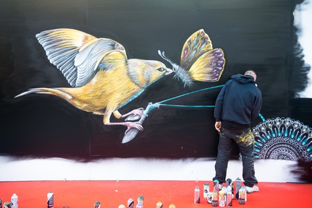 Paris, France - September 20, 2017: artist create graffiti drawing of bird and butterfly with spray paint on black wall. Street art, culture, painting concept.のeditorial素材