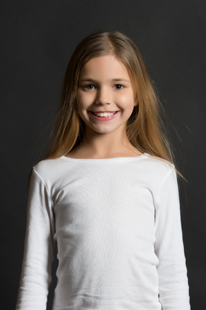 Girl with smile on cute face on dark background. Youth, skincare, health. Happy child, childhood concept. Beauty, look, hairstyle. Kid model smiling with long healthy hair.の写真素材
