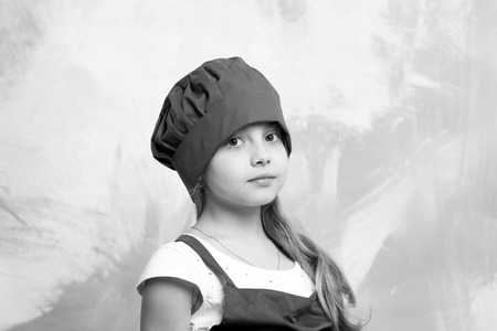 small baby girl or cute child with adorable face in red chef hat and cook apron on colorful abstract backgroundの写真素材