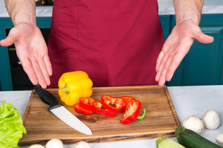 Hands point at pepper slices vegetable and ceramic knife on wooden cutting board. Vegetarian, health, diet concept. Food preparation, cooking.の写真素材