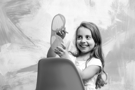 happy baby or small girl sitting on orange chair on colorful abstract background in summer glasses and tshirt with long blond hair, copy spaceの写真素材