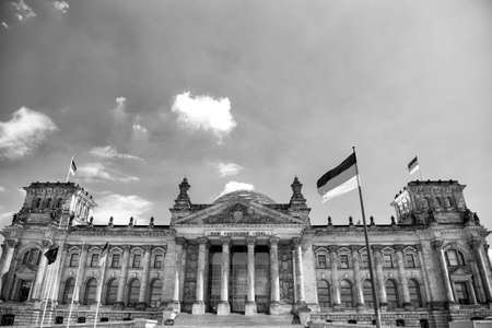 German flags waving in the wind at famous Reichstag building, seat of the German Parliament (Deutscher Bundestag), on a sunny day with blue sky and clouds, central Berlin Mitte district, Germanyのeditorial素材