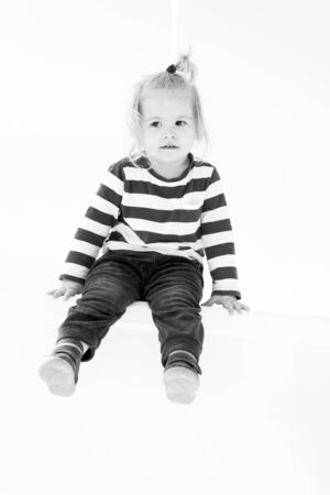 small baby boy or cute child with adorable face and blonde hair in stripped shirt and pants sitting isolated on white backgroundの写真素材