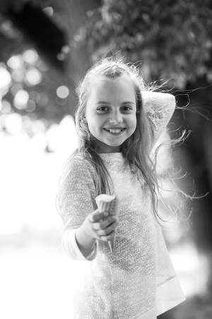 Girl with adorable smile, long blond hair with ice cream cone on sunny day on natural landscape. Food, snack, dessert eating outdoor. Summer vacation concept, black and whiteの写真素材