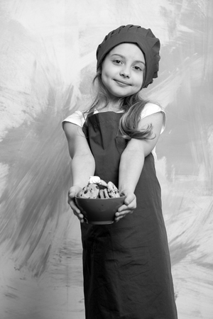 happy small girl holding chocolate cookies dessert in red cook hat and chef apron on colorful backgroundの写真素材