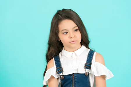 Girl with brown eyes on cute face on blue background. Kid model with long healthy brunette hair. Child, childhood concept. Beauty, look, hairstyle. Youth, skincare, healthの写真素材