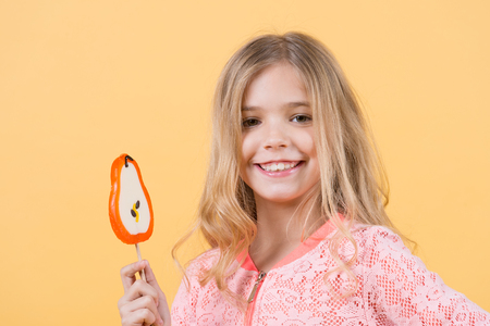 Happy childhood concept. Girl smile with lollipop on orange background. Child smiling with candy on stick. Food, dessert, snack. Punchy pastel trendの写真素材