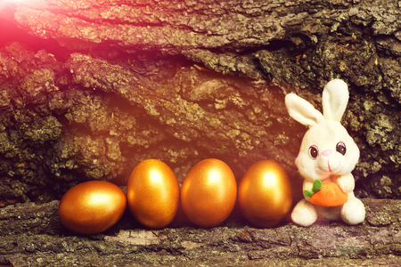 funny easter egg happy easter, rabbit toy with carrot, traditional golden eggs metallic color on tree bark background, farming, agriculture, luxury success, riches, treasure, retirement, antique artの写真素材