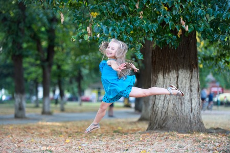 Little girl dancer jump in summer park. Child dance in blue dress, fashion. Happy childhood concept. Energy, activity, performance, ballet, gymnastics. Grace, beauty, fashion.の写真素材