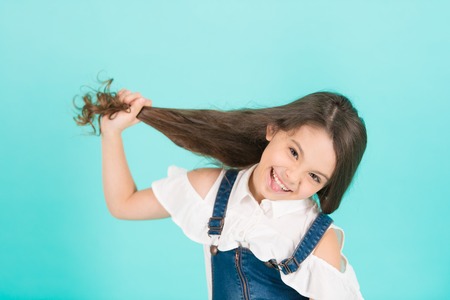 Beauty or hairdressing salon. Girl hold long hair on blue background. Child smile with healthy...