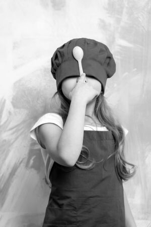 Girl cook hiding face with chef hat and wooden spoon on colorful abstract wall. Child and childhood. Cooking concept.の写真素材