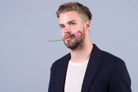 Man with flower in mouth, 8 march. Macho with bearded face, hair in jacket, holiday. Womens day, 8 march, spring. Love, romance, desire, proposal, date. Holiday celebration, party, copy spaceの写真素材