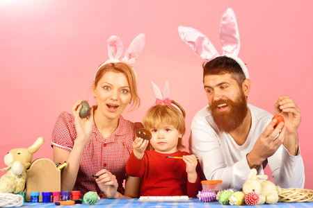 hapyy easter holidays eggs and bunny Family members wearing cute bunny ears. Man with beard, woman and kid with happy faces painting eggs on pink background. Easter celebration concept. Mother,の写真素材