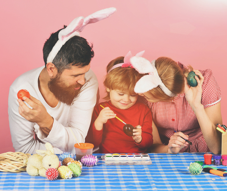easter eggs Man with beard, woman and kid with happy faces painting eggs on pink background. Family members wearing cute bunny ears. Easter celebration concept. Mother, father and daughterの写真素材