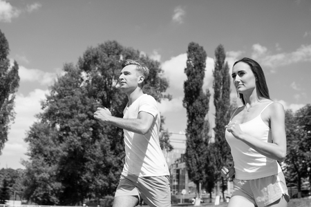 Couple running on arena track. Coach and trainer at workout. Runner on competition and future success. Man and woman sunny outdoor on blue sky. Sport and healthy fitness.の写真素材