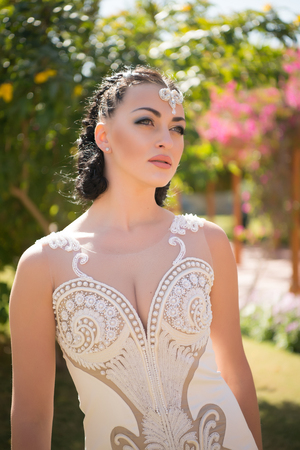 Woman with jewelry diadem on brunette hair. Sensual woman in white wedding dress with pearl beads. Bride with makeup face. Beauty girl with glamour look and makeup. Fashion model in summer garden.の写真素材