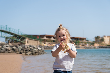 Little boy smile with shell on sea beach. Child play with seashell on sunny seascape. Freedom, discovery and adventure. Summer vacation on sea. Happy childhood concept.の写真素材