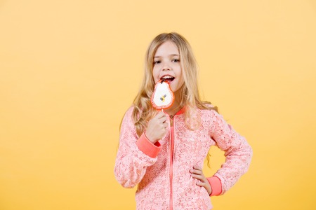 Beautiful cute little girl eat lollipop on orange background, copy space