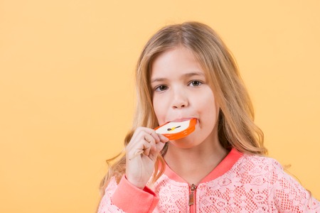 Child eat candy on stick, food. Little girl with lollipop, snack. Food, snack, dessert, confectionery. Kid beauty, hair, fashion, look. Punchy pastel trend, copy spaceの写真素材