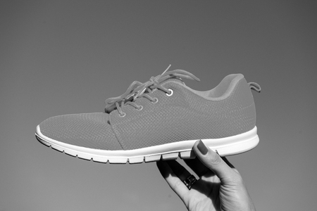 Sports shoes sneakers on blue sky background. Sports in the open air. woman hand holding orange sneakers fitness and healthの写真素材