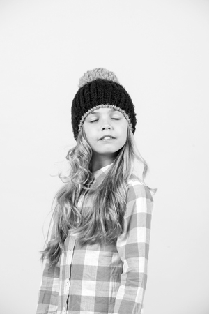 Kid with closed eyes on cute face, long blond hair in hat and plaid shirt pose on orange background. Child fashion, beauty, style concept.の写真素材