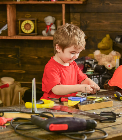 Kid boy play as handyman. Child cute and adorable playing with tools as builder or repairer, repairing or handcrafting. Toddler on busy face plays with tools at home in workshop. Childhood conceptの写真素材