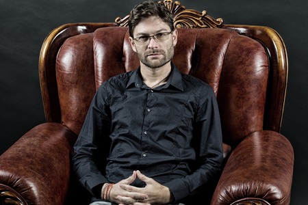 Macho relax in brown leather armchair. Man with beard on unshaven face. Bearded man wear shirt and glasses. Barber salon and skincare. Fashion accessory and furniture, vintage filter.の写真素材