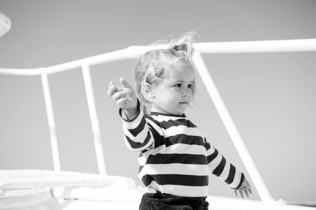 Travel destination, cruise, travelling. Child with blond hair on yacht on sunny day. Adventure, discovery, wanderlust. Summer vacation concept. Boy in sailor shirt on blue sky.の写真素材