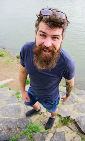 Hipster on cheerful face with fashionable sunglasses. Guy looks cool with stylish sunglasses. Fashion concept. Man with beard and mustache wears sunglasses, water surface on backgroundの写真素材