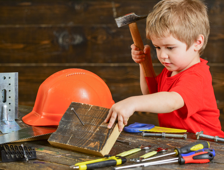 Cute kid hammering nails in wooden board. Little repairman in workshop. Blond boy doing manual laborの写真素材