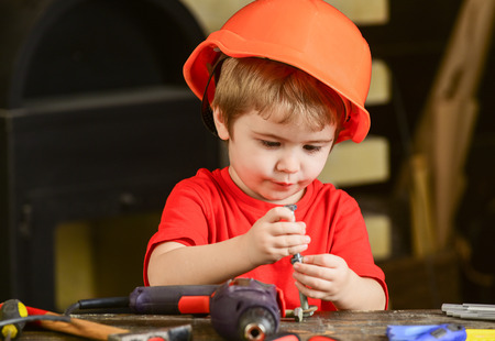 Child in hard hat, helmet playing with hex bolts as builder or repairer, handcrafting. Toddler on busy face plays with bolts at home in workshop. Handcrafting concept. Kid boy play as handymanの写真素材