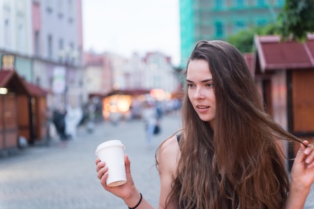 Woman with takeaway drink walk on street. Sexy woman hold disposable coffee cup. Beauty girl with long hair and natural makeup. Coffee or tea mood. Drink and food during summer vacation or travelling.の写真素材