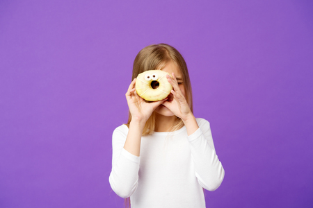 Sweet mood. Child look in donut on violet background. Little girl with glazed ring doughnut on purple background. Kid with junk food. Food and dessert. Childhood and childcare, copy space.の写真素材
