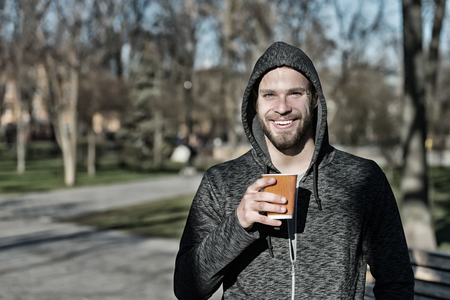 Coffee or tea mood. Happy macho in hood hold disposable coffee cup in sunny park. Bearded man smile with takeaway drink on fresh air. Drink and food outdoor. Morning tea for breakfast, vintage.の写真素材