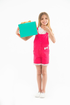 Little child point finger at shopping bag isolated on white. Happy girl smile with paper bag. Kid shopper in fashion jumpsuit. Holidays and celebration. Shopping at black friday. All I got on saleの写真素材