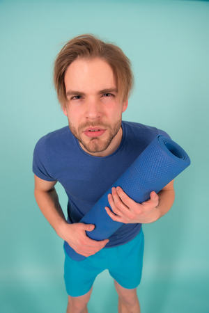 Sportsman look with serious face. Man hold yoga mat. Fashion athlete in blue tshirt and shorts. Gym equipment for training and workout. Yoga or pilates and sport activity.の写真素材