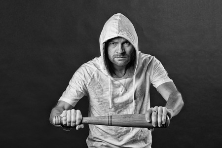 Bearded man threaten with bat weapon. Hooligan wear hood in hoodie tshirt. Gangster guy hold...