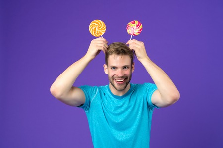 Funny man with lollipops on head on violet background. Macho smile with candies on sticks on purple...