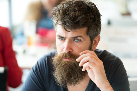 Man with beard and mustache sits outdoor at cafe terrace. Bearded man on concentrated face touches mustache. Hipster with beard looks thoughtful or troubled. Thoughtful mood conceptの写真素材