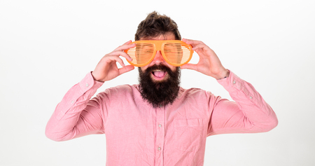 Hipster looking through of giant striped sunglasses. Man with beard and mustache on happy face wears funny eyeglasses, white background. Guy with beard in cheerful mood. Optics and glasses conceptの写真素材